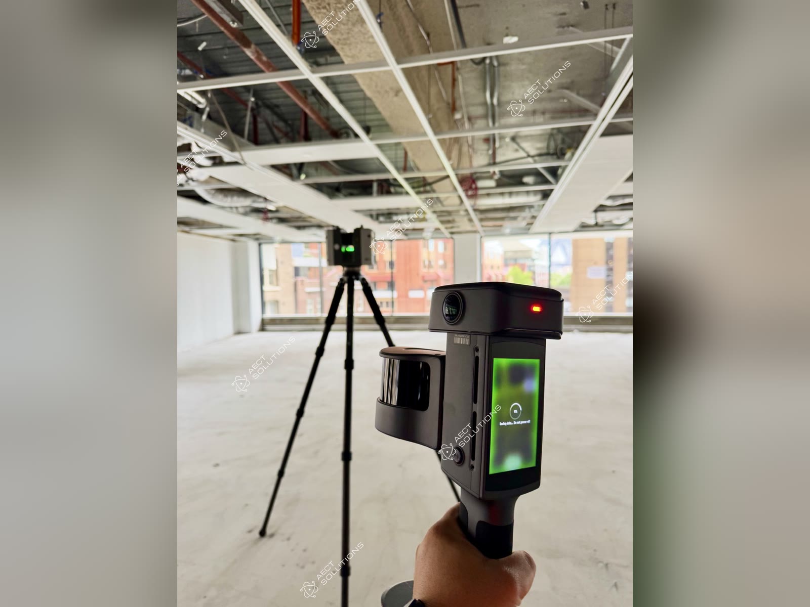 XGRIDS Lixel L3 handheld SLAM scanner in the foreground with a Leica RTC terrestrial laser scanner on a tripod behind it, during a SLAM and TLS data fusion test in an open-plan office fit-out